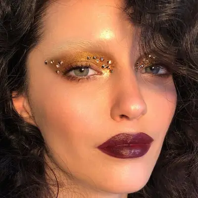 Model with burgundy lipstick, bleached eyebrows, and gold eyeshadow with gems