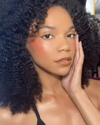 A woman wearing sunset blush with glossy caramel lips and gold eyeshadow
