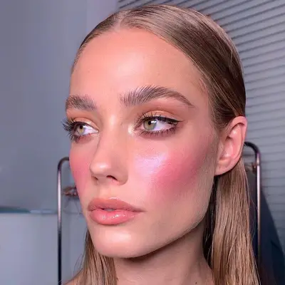 Model with radiant makeup look with flushed pink blush, glossy lips, and neutral eyeshadow