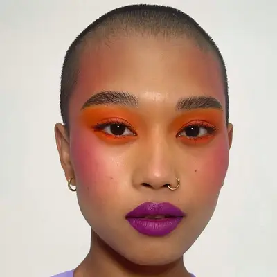 Model with orange eyeshadow, pink blush, and purple lipstick