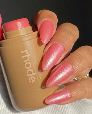A sparkly pink manicured hand holds a tube of Rhode Blush in Sprinkle.
