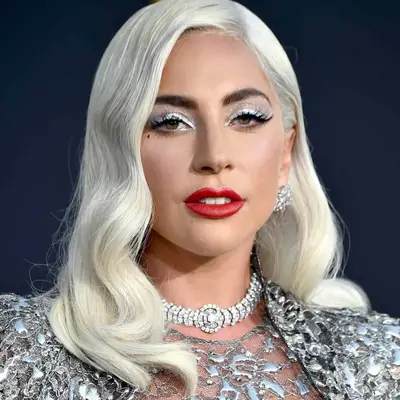 Lady Gaga wears silvery glitter white eyeshadow, red lipstick, a beauty mark, and a platinum blowout