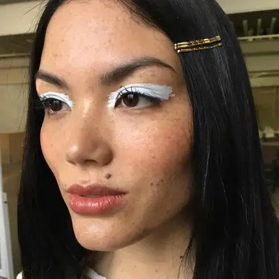 Woman with abstract opaque white eyeshadow, subtle cheek and lip, and gold bobby pins