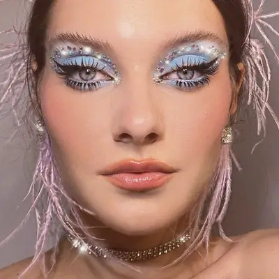 Model wears blue eyeshadow with gem stones and pink feather earrings