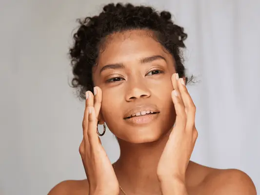 A close up of a curly haired model holding the temples of her face.