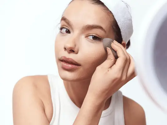 Close up of a model applying face makeup under the eye with an egg-shaped beauty sponge.