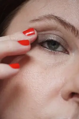 model is applying a shimmering taupe shadow to the center of the eyelid and outer corner with finger
