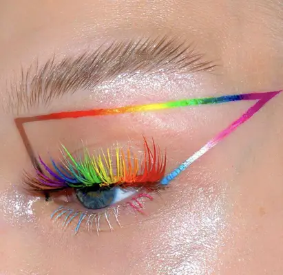 model is wearing rainbow eyelashes and a graphic triangle around the eye showcasing the progress pride flag colors