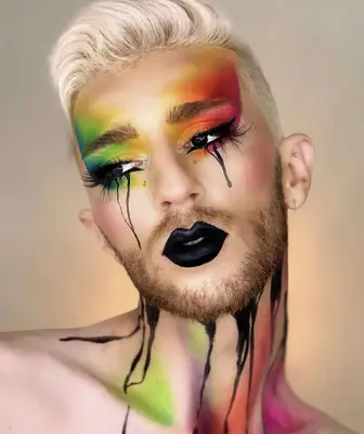 model is wearing rainbow colors on the eyes that appear airbrushed, with black tear streaks drawn on the face and black lipstick, the neck is displaying black streaks with rainbow accents
