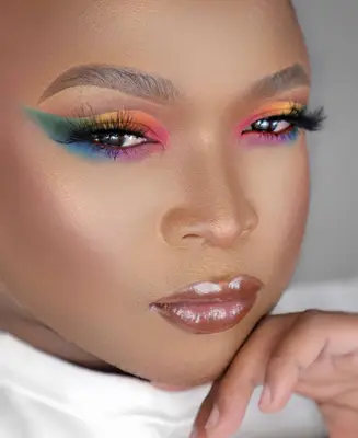 model is wearing rainbow hues on the eyes in a wing shape, false lashes and glossy nude lips
