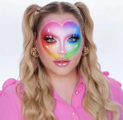 Model is wearing airbrushed makeup in the shape of a rainbow heart on the forehead extended down to the cheeks and nose