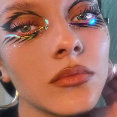 a model with stud and iridescent face decals around their eyes 