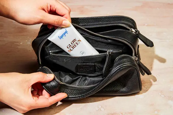 A person taking sunscreen out of the Royce New York Double Zip Leather Toiletry Bag