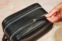 A person unzipping the Royce New York Double Zip Leather Toiletry Bag