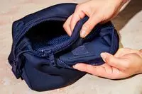 A person velcro-ing a pocket on the Dagne Dover Hunter Toiletry Bag