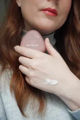 model is holding rare beauty hand cream and there is a visible swatch of hand cream on the hand