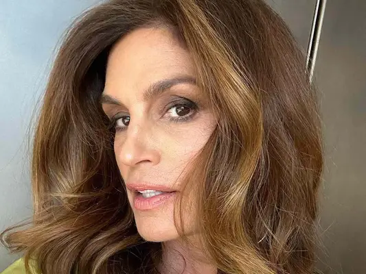 Cindy Crawford wears a subtle makeup look with foundation, pink lipstick, and a brown smoky eye