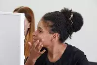 Reflection in lighted mirror of person applying skin tint to face