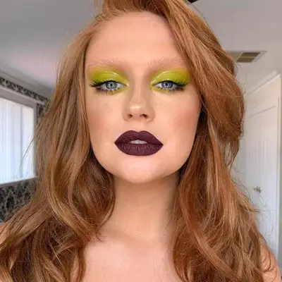 Woman with blue eyes, dark mauve lip, and a wet green eye look.