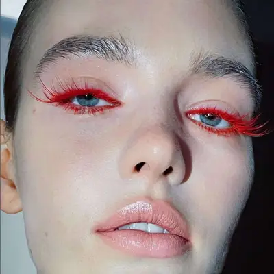 Woman with blue eyes and exaggerated red eyelashes and eyeliner.