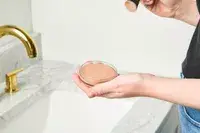 A person applies Saie Sun Melt Natural Cream Bronzer with a makeup brush