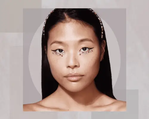 AAPI Woman Wearing Glittery Makeup with Gems Around Her Eyes on an Abstract Background