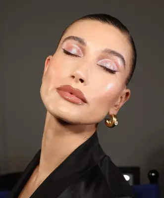 Hailey Bieber posing with her eye closed wearing a shimmering and holographic lilac eyeshadow look