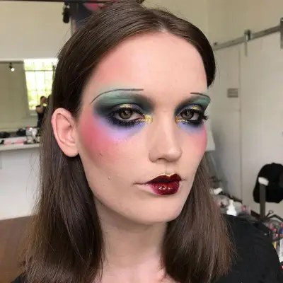 Model wears abstract colorful 1920s eye makeup look, thin eyebrows, and red heart-shaped lips