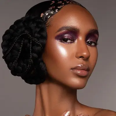 Model wears a purple smoky eye, radiant skin, glossy lips, and a 1920s updo