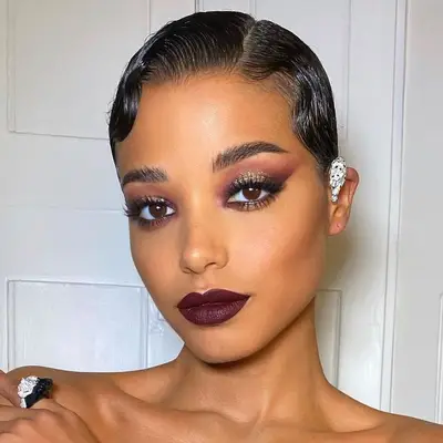 Ella Balinska wears a glittery plum smoky eye, berry lips, and sleek finger waves