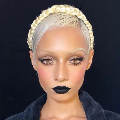 Model with platinum hair wears a 1920s-inspired makeup look with thin brows, lashes, and dark lips