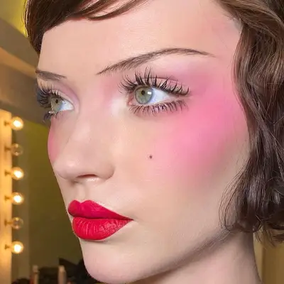 Model wears a 1920s makeup look with thin brows, dramatic lips and blush, and feathered lashes