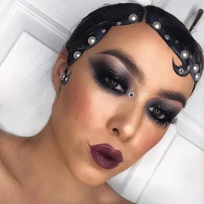 Model wears smoky eyeshadow, purple lipstick, and pearl-encrusted slicked hairstyle