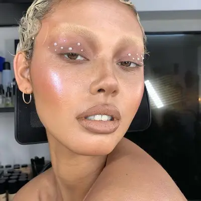 Model wears neutral makeup with pearls on eyelids and radiant highlighter on cheeks
