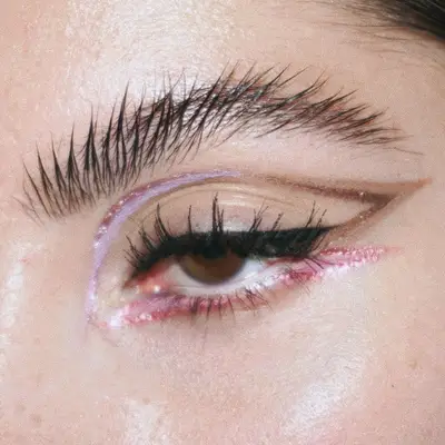 Woman wears multicolored pink and brown graphic eyeliner with glitter