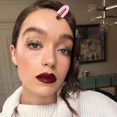 Model wears golden glitter eye makeup and burgundy lipstick