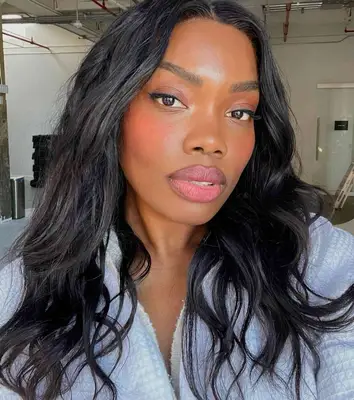 model wears soft pink tones of blush and lipstick with thin black eyeliner