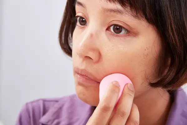 Person applying foundation with a beauty blender on to their cheek 