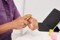 Person dispensing Kosas Revealer Skin-Improving Foundation SPF 25 onto back of hand with nearby laptop