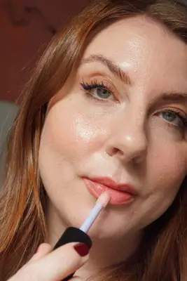 model is applying lip gloss to the center of the bottom lip with an applicator