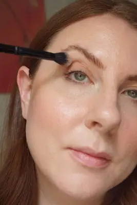 model applying eyeshadow to lids with a fluffy shadow brush