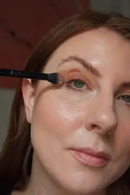 model applying eyeshadow to the lid with a fluffy eyeshadow brush