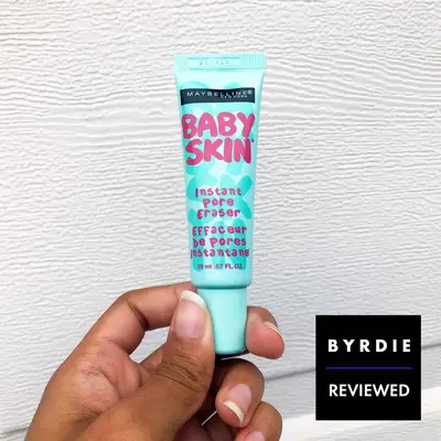 Hand holding a tube of Maybelline baby skin instant pore eraser with a white background 