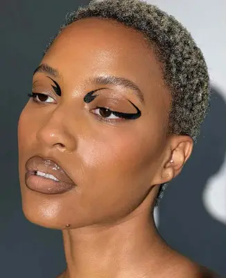 model is wearing abstract black eyeliner around the perimeter of the eyes, with nude glossy lips outlined with darker lipliner
