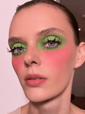 model wears lime green eyeshadow and bright pink cheeks with 60s inspired spidery eyelashes 