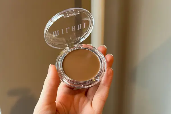 A person holds up a Milani Cheek Kiss Cream Bronzer compact 