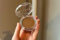 A person holds up a Milani Cheek Kiss Cream Bronzer compact 