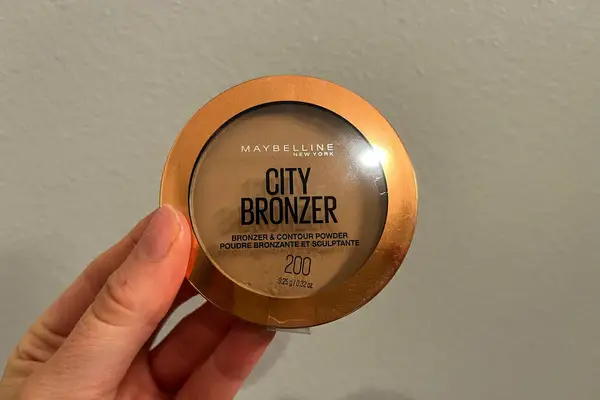 A person holds up a Maybelline New York City Bronzer Powder Makeup compact
