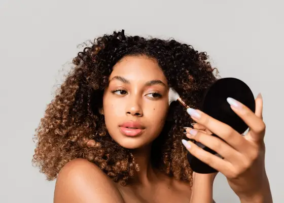 Woman with curly hair applying makeup to her face using a foundation brush