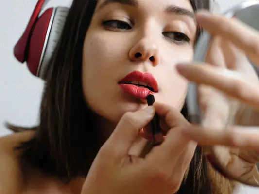 Woman Wearing Headphones Putting On Lipstick